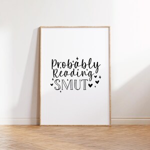 Puede incluir: Una impresi&oacute;n enmarcada con el texto "Probably Reading SMUT" en fuente cursiva negra con peque&ntilde;os corazones y estrellas alrededor del texto.