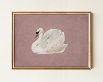 May include: A framed print featuring a watercolor painting of a swan. The swan is white with a black beak and red accents, set against a muted mauve background. The artwork is enclosed in a gold-colored frame, suitable for wall decor.