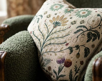 May include: A square throw pillow featuring a cream-colored fabric base with a woven botanical pattern. The design includes stylized flowers and leaves in shades of green, gold, purple, and deep red, creating a detailed floral tapestry effect.