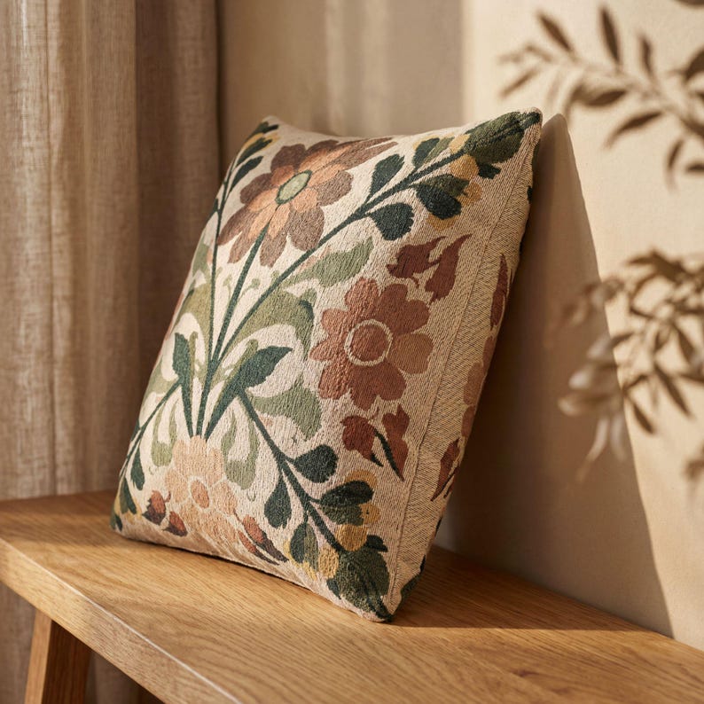 May include: A square throw pillow featuring a woven floral pattern in shades of terracotta, sage green, and cream. The design displays large stylized flowers and leafy stems across the front surface, creating a textured and detailed botanical appearance.