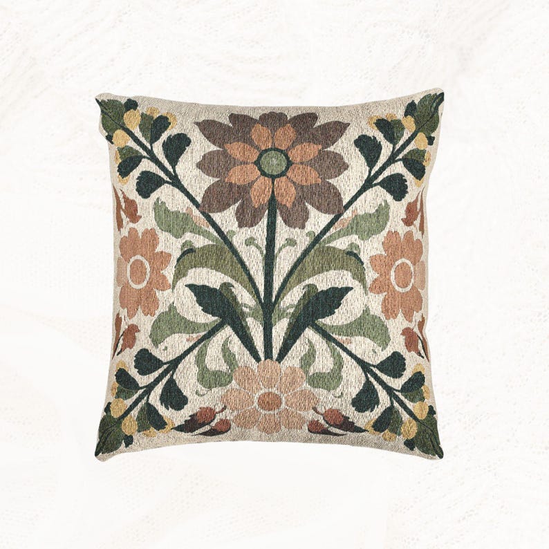 May include: A square throw pillow featuring a woven tapestry design with a central floral motif. The pattern displays large brown, peach, and light green flowers surrounded by dark green leaves and stems against a light beige textured background.