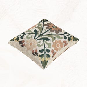May include: A square throw pillow featuring a woven floral pattern on a light beige background. The design includes stylized flowers and leaves in shades of dark green, muted orange, brown, and pale yellow, creating a symmetrical botanical motif.