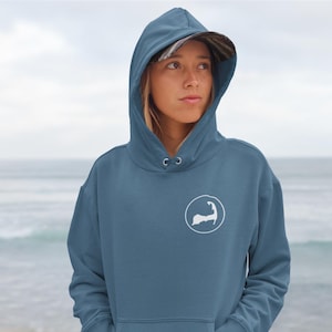 Op de afbeelding: Een blauw hoodie met een witte omtrek van de staat Cape Cod in een cirkel op de voorkant.