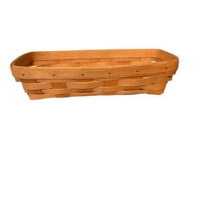 Puede incluir: Una cesta rectangular tejida en color marrón claro. La cesta tiene un borde redondeado y está construida con tiras de madera entrelazadas. Pequeños remaches oscuros aseguran el borde.