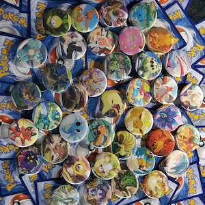 May include: A collection of colorful Pokemon character button pins. The pins feature various Pokemon characters, including Pikachu, Charmander, Bulbasaur, Squirtle, and many more. The pins are arranged in a random pattern on a blue background.
