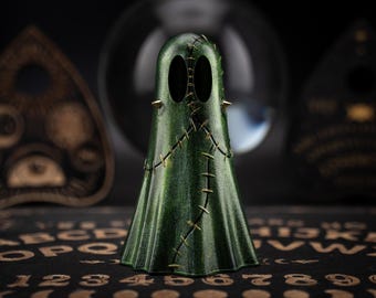 May include: A green ghost figurine with gold stitching and spikes. The ghost is standing on a black surface with gold letters and numbers.