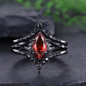 May include: A black ring set with a central, marquise-cut, deep red gemstone. The ring is embellished with smaller black gemstones and detailed patterns. The band has a layered design, offering a striking and sophisticated appearance.