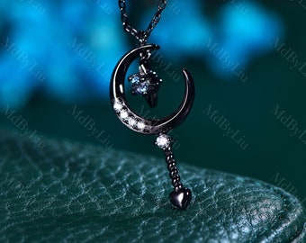 May include: A black necklace with a crescent moon pendant featuring a small blue gemstone and a heart-shaped charm at the end of a chain. The pendant is adorned with small white gemstones.