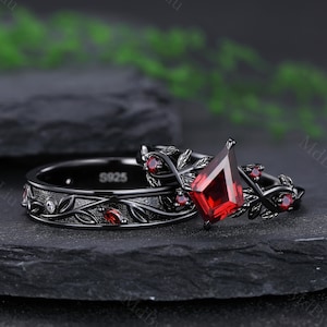 Puede incluir: Un juego de anillos negro y rojo con una gran piedra roja y diseños intrincados de hojas. El anillo está grabado con el número "S925".