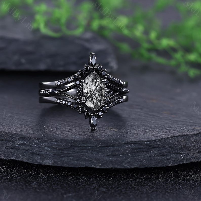Pode incluir: Um conjunto de an&eacute;is pretos com uma pedra central de formato geom&eacute;trico com um padr&atilde;o em preto e branco. O anel &eacute; rodeado por pedras pretas menores e tem uma banda a condizer. O anel &eacute; exibido numa superf&iacute;cie escura e texturizada.