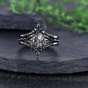 Pode incluir: Um conjunto de an&eacute;is pretos com uma pedra central facetada e alongada com inclus&otilde;es pretas. O anel &eacute; ladeado por duas bandas, cada uma adornada com pequenas pedras pretas. O design tem uma est&eacute;tica g&oacute;tica ou vintage.