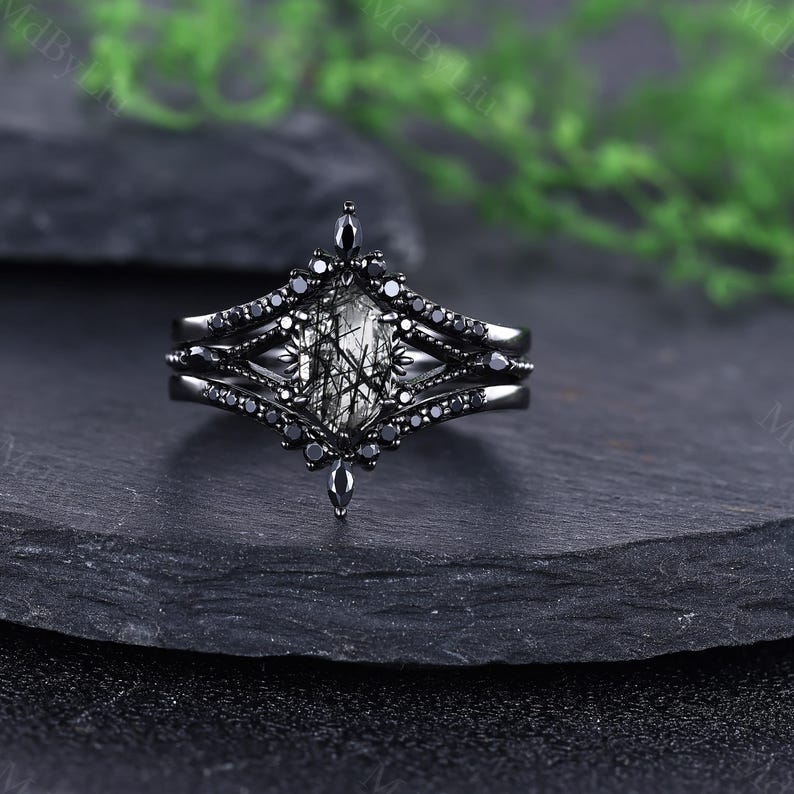 Pode incluir: Um conjunto de an&eacute;is pretos com uma pedra central facetada e alongada com inclus&otilde;es pretas. O anel &eacute; ladeado por duas bandas, cada uma adornada com pequenas pedras pretas. O design tem uma est&eacute;tica g&oacute;tica ou vintage.