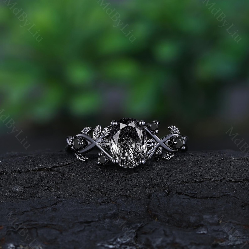 May include: Black engagement ring with a large oval-shaped gemstone and black diamond accents. The ring features a delicate leaf design on the band.