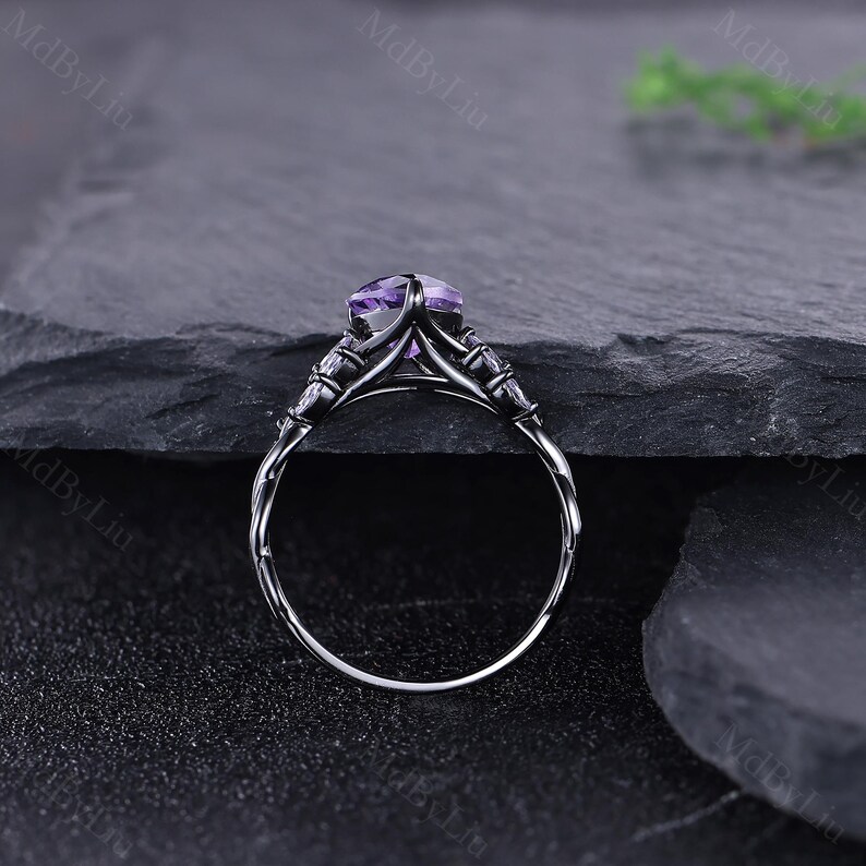 May include: A silver ring featuring a large, oval-cut purple gemstone. The ring has an intricate design with smaller accent stones and a twisted band. The ring is set against a dark, textured background.