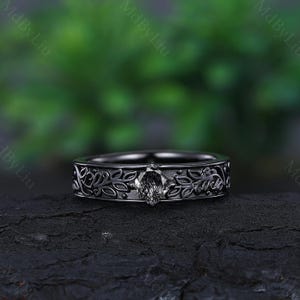 May include: A black ring with a floral design and a single diamond in the center.