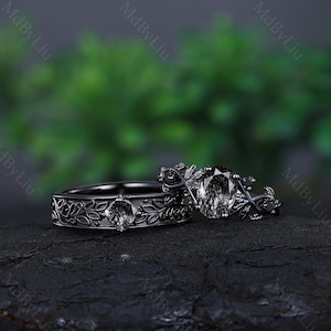 May include: A black wedding ring set with a floral design and a large, clear gemstone. The rings are on a dark, textured surface.
