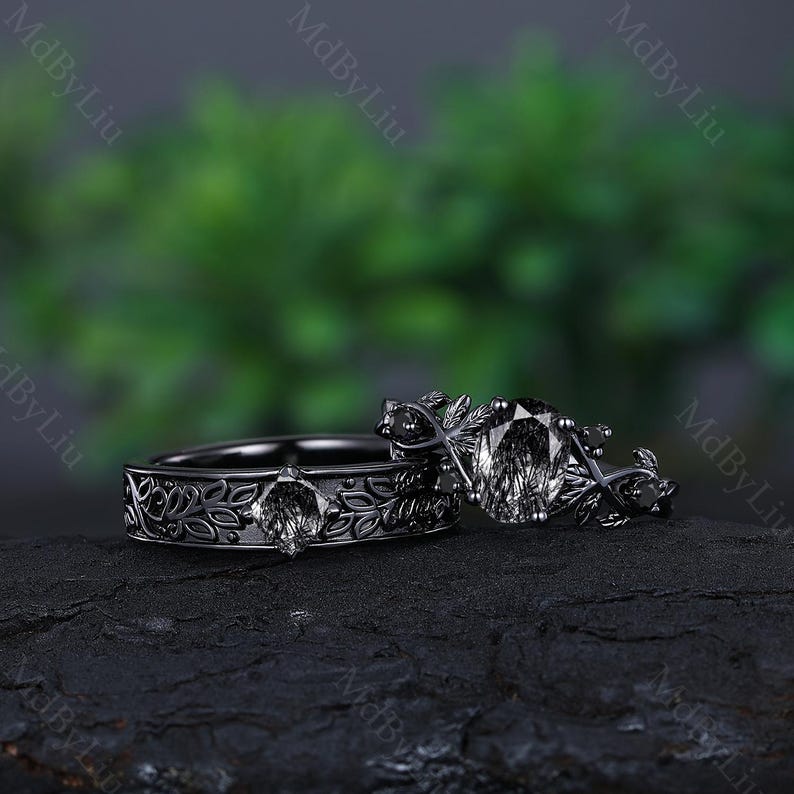 May include: A black wedding ring set with a floral design and a large, clear gemstone. The rings are on a dark, textured surface.