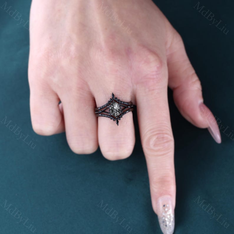 Pode incluir: Um conjunto de an&eacute;is de noivado pretos com uma pedra central em forma de diamante com um tom verde claro, rodeada por pedras pretas menores. O anel tem um design &uacute;nico e ornamentado. O conjunto inclui uma banda a condizer.