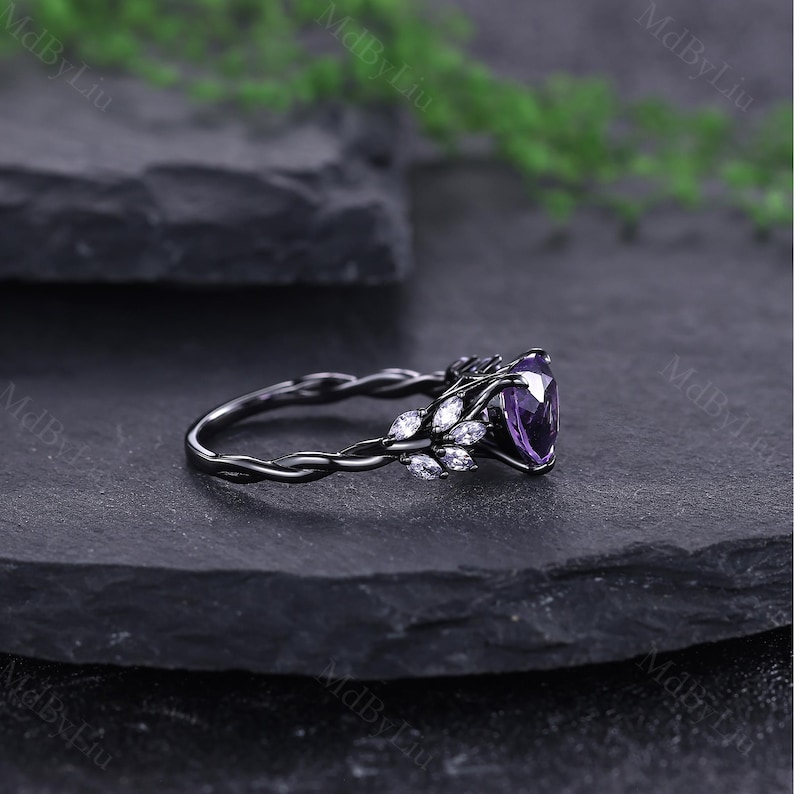 May include: A black ring featuring a large, heart-shaped purple gemstone. The ring has a twisted band and is decorated with small, white accent stones. The design incorporates a floral theme, with the gemstones arranged in a leaf-like pattern.