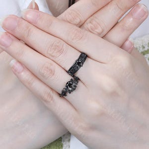 May include: A pair of black engagement rings with intricate floral designs and black gemstones. The rings are worn on a person's finger.