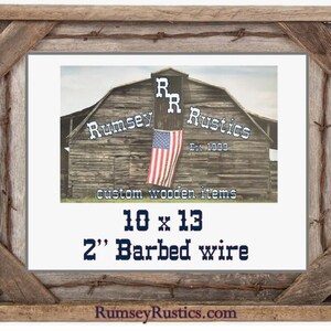 May include: A rustic wooden picture frame with a distressed gray finish and barbed wire accents. The frame is 10 inches by 13 inches and has a 2 inch wide barbed wire border. The frame is made by Rumsey Rustics, a company that specializes in custom wooden items.