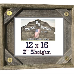 May include: A rustic wooden picture frame with a gray background and a red, white, and blue American flag. The frame is decorated with four brass bullet casings. The text "Rumsey R Rustics Est. 1999 custom wooden items 12 x 16 2" Shotgun" is printed on the frame.
