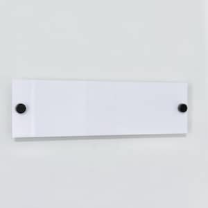 May include: A rectangular white sign with rounded corners is mounted on a white wall. Two black circular fasteners secure the sign to the wall, one on each end. The sign is clean and minimalist.