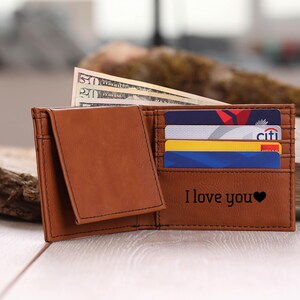 May include: A brown leather wallet with a flap closure and multiple card slots. The wallet has the words "I love you" and a heart symbol engraved on the front.