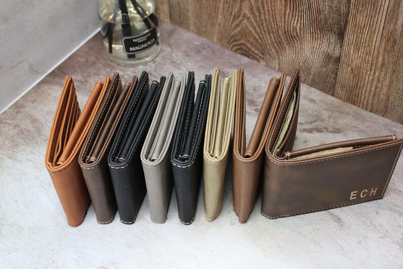 Puede incluir: Ocho carteras de cuero en varios colores, incluyendo marr&oacute;n, negro, gris y beige. Las carteras est&aacute;n dobladas y alineadas en una fila. La &uacute;ltima cartera tiene las iniciales "ECH" grabadas en la parte delantera.