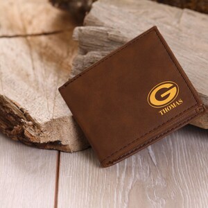 May include: A brown leather wallet with a gold Green Bay Packers logo and the name "THOMAS" embossed on the front.