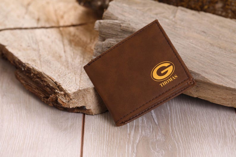 May include: A brown leather wallet with a gold Green Bay Packers logo and the name "THOMAS" embossed on the front.