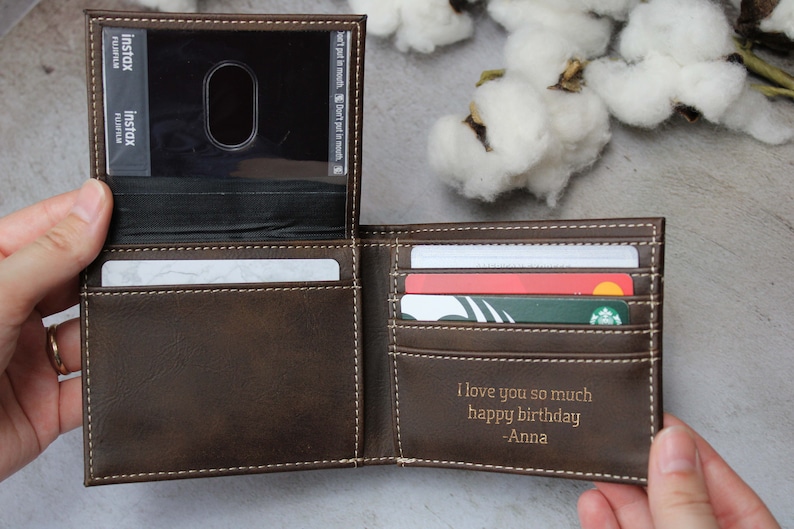 Puede incluir: Una cartera de cuero marr&oacute;n con una inscripci&oacute;n personalizada que dice "Te quiero mucho feliz cumplea&ntilde;os -Anna". La cartera tiene m&uacute;ltiples ranuras para tarjetas y una ventana de pl&aacute;stico transparente para una tarjeta de identificaci&oacute;n.
