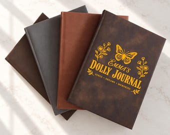 May include: A stack of four rectangular journals with smooth covers in shades of dark brown, medium brown, and gray. The top journal features a yellow graphic of a butterfly and flowers with the text EMMA'S DOLLY JOURNAL SONGS DREAMS MEMORIES.