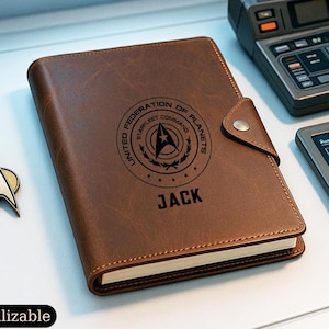 May include: A brown leather journal featuring the United Federation of Planets Starfleet Command logo and the name JACK embossed on the cover. The journal has a snap closure and is accompanied by a metallic Starfleet insignia pin.