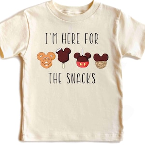 May include: A light beige t-shirt with the text "I'm here for the snacks" printed in black. The shirt features a row of four cartoon Mickey Mouse-shaped snacks.