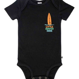 K&ouml;nnte beinhalten: Schwarzer Kurzarm-Body mit einem Grafikdruck eines Surfbretts und dem Text "LITTLE SURFER DUDE" in Regenbogenfarben.