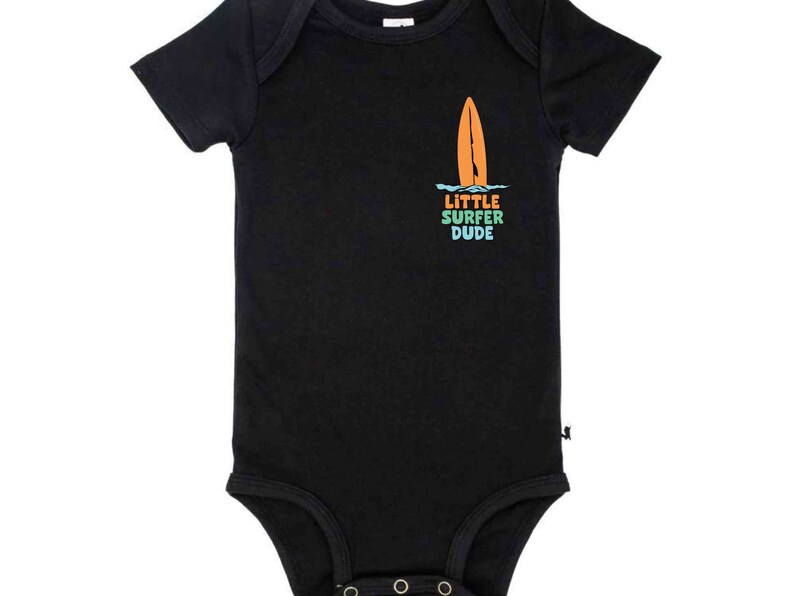 K&ouml;nnte beinhalten: Schwarzer Kurzarm-Body mit einem Grafikdruck eines Surfbretts und dem Text "LITTLE SURFER DUDE" in Regenbogenfarben.