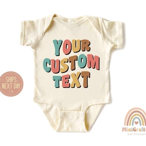 May include: A cream colored baby onesie with the text "YOUR CUSTOM TEXT" in colorful, retro-style letters. The letters are in shades of pink, yellow, blue, and brown.