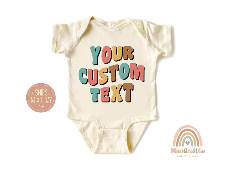 May include: A cream colored baby onesie with the text "YOUR CUSTOM TEXT" in colorful, retro-style letters. The letters are in shades of pink, yellow, blue, and brown.