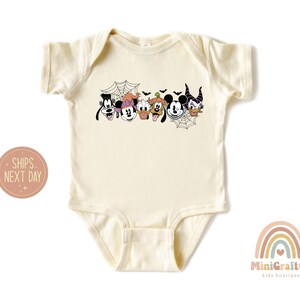 K&ouml;nnte beinhalten: Ein cremefarbener Baby-Strampler mit einem Halloween-Motiv, das Mickey Mouse, Minnie Mouse, Goofy, Pluto und Maleficent zeigt. Die Figuren sind in einer Reihe angeordnet, mit einem Spinnennetz und Flederm&auml;usen im Hintergrund.