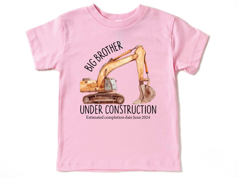 Pode incluir: Camiseta rosa claro para crian&ccedil;a com uma ilustra&ccedil;&atilde;o de uma escavadeira de constru&ccedil;&atilde;o. O texto diz "BIG BROTHER UNDER CONSTRUCTION" com uma data de conclus&atilde;o estimada em junho de 2024.