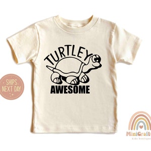 May include: A cream colored t-shirt with a black turtle graphic and the text "TURTLEY AWESOME".