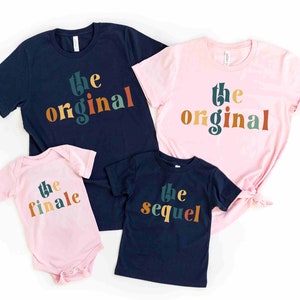 May include: A set of four t-shirts with the text "the original", "the finale", "the sequel" in colorful, retro-style lettering. The shirts are in navy blue and pink.
