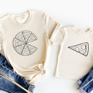 May include: Two cream-colored t-shirts with a pizza graphic. The larger shirt has a whole pizza with a slice missing. The smaller shirt has a single slice of pizza.