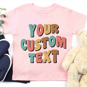 May include: Pink t-shirt with the text "YOUR CUSTOM TEXT" in colorful, bold letters.