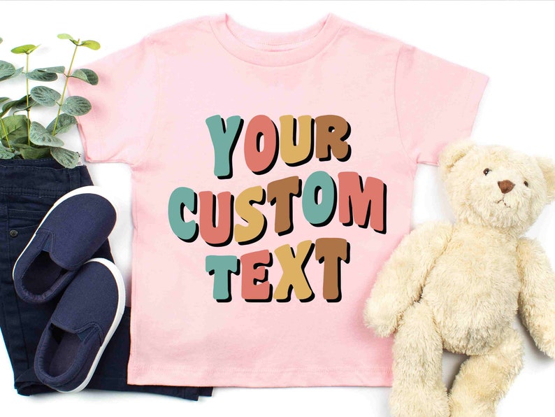 May include: Pink t-shirt with the text "YOUR CUSTOM TEXT" in colorful, bold letters.