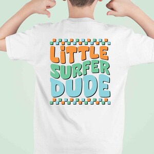 K&ouml;nnte beinhalten: Wei&szlig;es T-Shirt mit dem Text "little surfer dude" in bunten Blockbuchstaben.