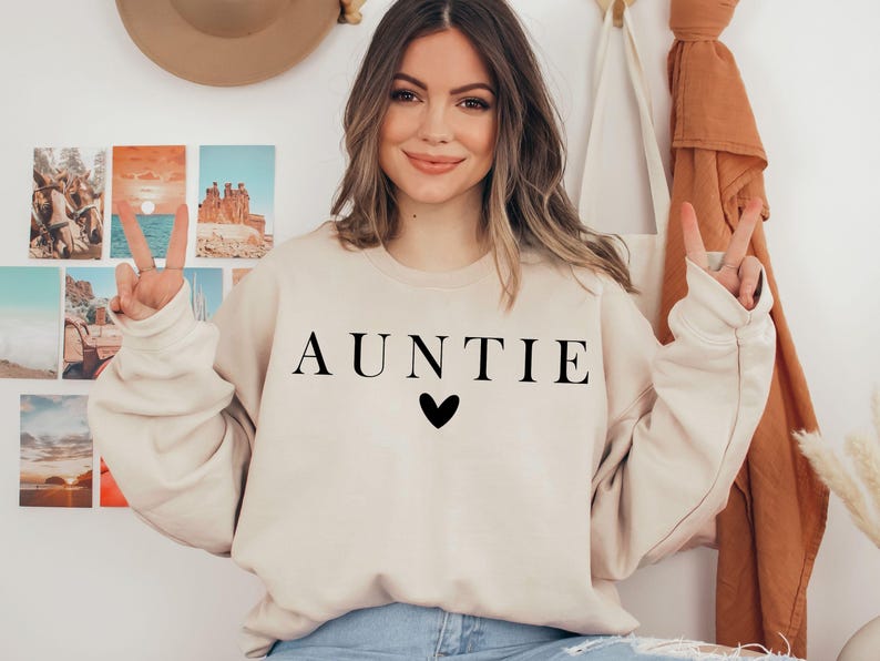 May include: A beige sweatshirt with the word "AUNTIE" printed in black letters and a small black heart below the word.