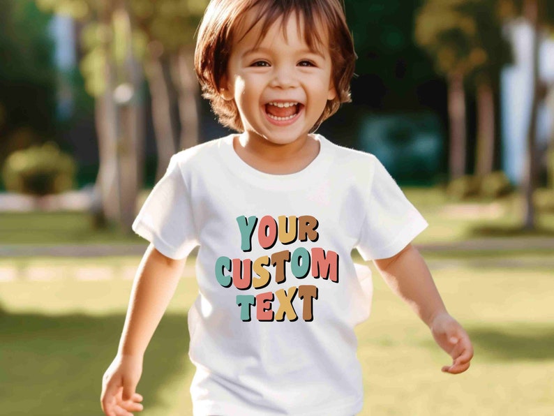 May include: A white t-shirt with a colorful graphic that says "YOUR CUSTOM TEXT". The text is in a retro style font with each letter in a different color. A young child is wearing the shirt and smiling.