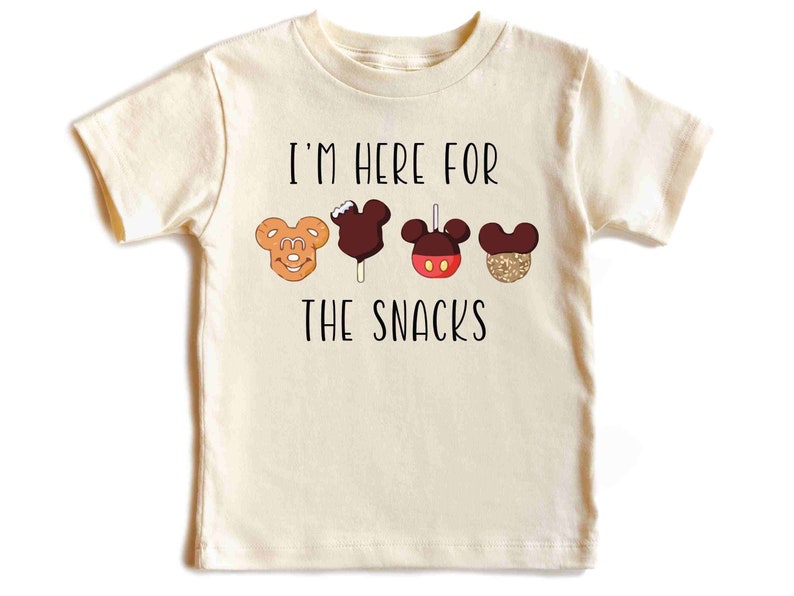 May include: A light beige t-shirt with the text "I'm here for the snacks" printed in black. The shirt features a row of four cartoon Mickey Mouse-shaped snacks.